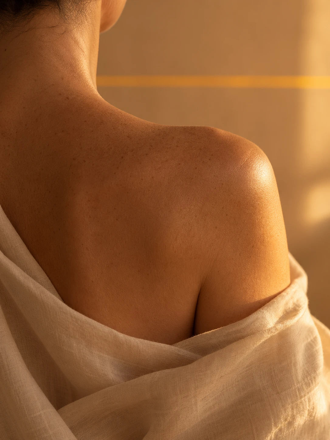 Body fragment of a woman in a bone-cream linen robe, tungsten window light, the Tideline trio softly out of focus