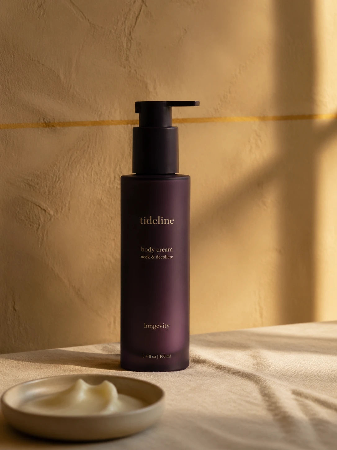 Tall plum-ink Tideline daily cream pump bottle in tungsten light, with cream dollop in foreground