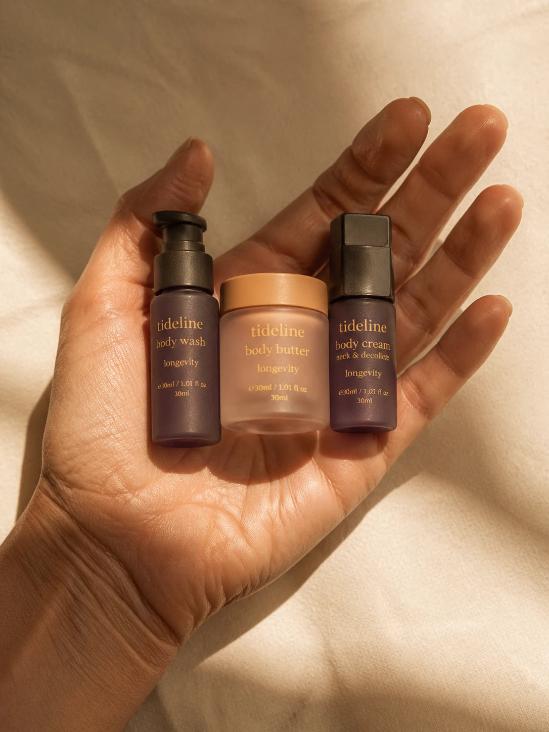 Three Tideline travel-size bottles held in an open palm, body fragment for scale